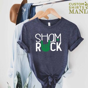 Peut inclure: Un t-shirt bleu fonc&eacute; avec le texte "Shamrock" et un symbole de main rock and roll vert.