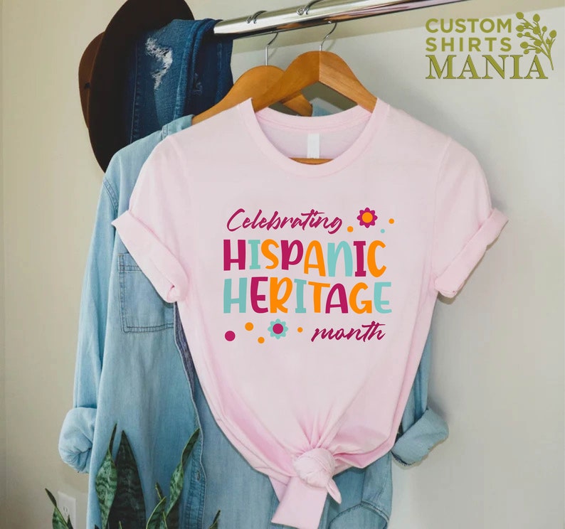 May include: Pink t-shirt with the text "Celebrating Hispanic Heritage month" in colorful letters with small flower accents.