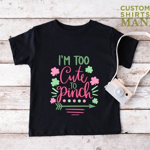 May include: Black t-shirt with a pink and green graphic that says "I'm Too Cute To Pinch".