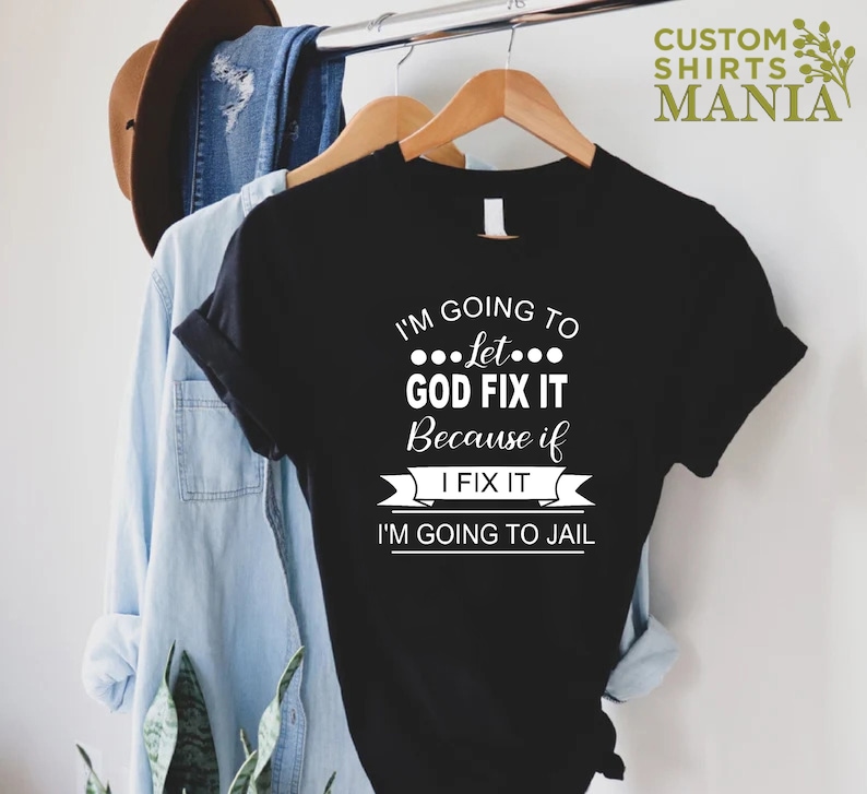 May include: Black t-shirt with white text that reads "I'm going to let... GOD FIX IT because if I FIX IT I'M GOING TO JAIL".