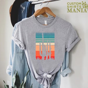 May include: A gray t-shirt with a retro-style graphic of a cactus silhouette against a colorful striped background. The text "CUSTOM SHIRTS MANIA" is visible in the top right corner of the image.