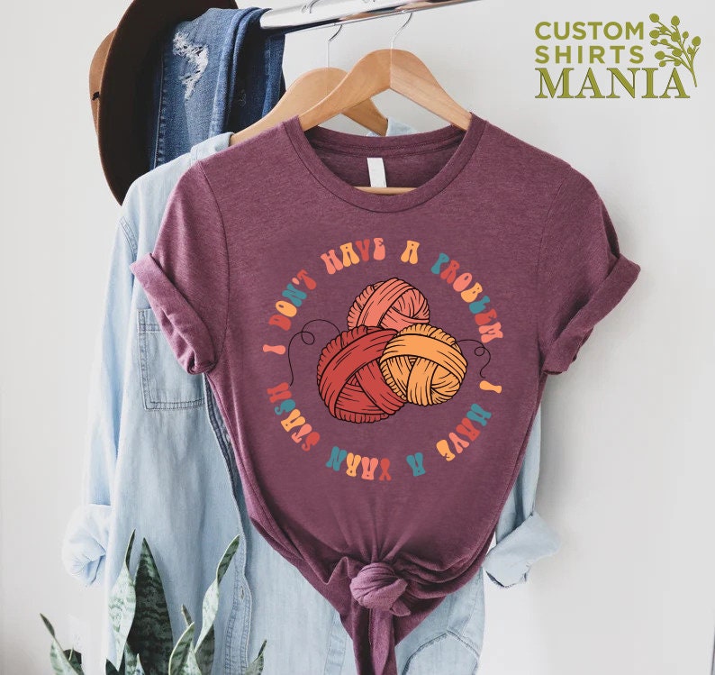 May include: A maroon t-shirt with a graphic of yarn balls and the text "I don't have a problem I have a yarn stash".