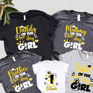 May include: Five t-shirts with bee-themed designs. The shirts say "Daddy of the bee-day girl", "Mommy of the bee-day girl", "Brother of the bee-day girl", "Sister of the bee-day girl", and "My 1st bee day Olivia".