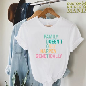 Op de afbeelding: Wit T-shirt met een kleurrijke afbeelding met de tekst "Family Doesn't Only Happen Genetically".