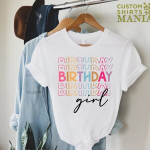 May include: White t-shirt with the text "Birthday girl" in rainbow colours. The text is stacked and the word "Birthday" is repeated multiple times.