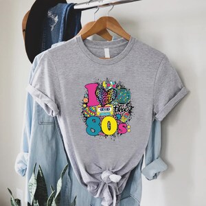 May include: Gray t-shirt with a graphic design of a heart with a leopard print, a cassette tape, a disco ball, and the text "I love the 80's".