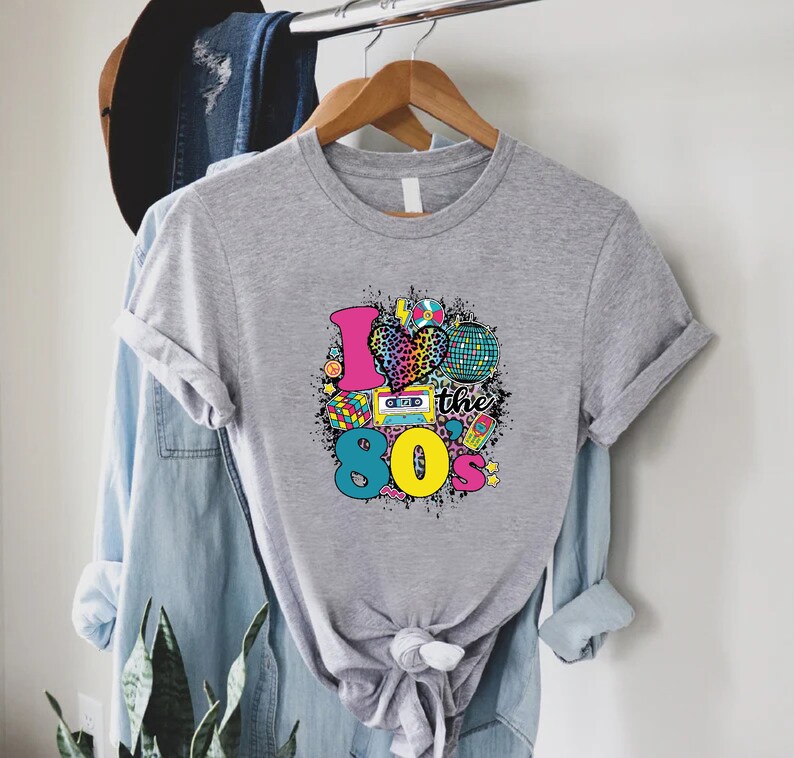 May include: Gray t-shirt with a graphic design of a heart with a leopard print, a cassette tape, a disco ball, and the text "I love the 80's".