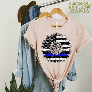 May include: A pink t-shirt featuring a black and white sunflower design. The sunflower has a blue line running through the centre, representing the thin blue line.