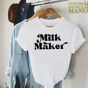 May include: White t-shirt with black text that reads "Milk Maker" in a retro font.