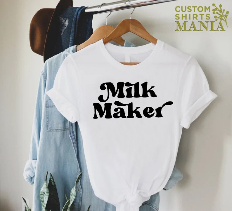 May include: White t-shirt with black text that reads "Milk Maker" in a retro font.