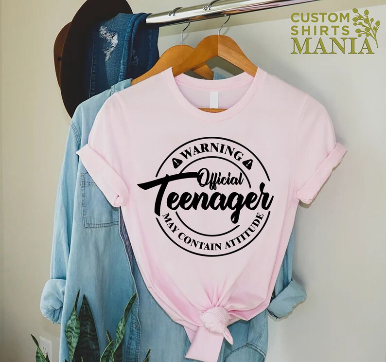 May include: Pink t-shirt with a black circle graphic that says "Warning Official Teenager May Contain Attitude".
