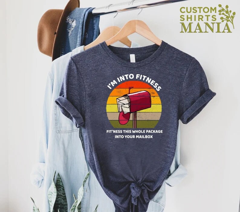 May include: A navy blue t-shirt with a retro-style graphic of a red mailbox with the text "I'm into fitness" and "Fit'ness this whole package into your mailbox".