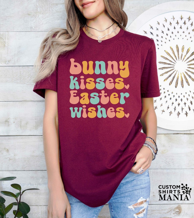 May include: A maroon t-shirt with the text "bunny kisses Easter wishes" in a retro font with pastel colors.