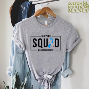 May include: Gray t-shirt with a black box that says "Support Squad" with a blue ribbon and the words "Diabetes Awareness" underneath.