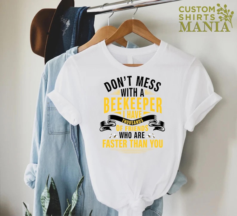 May include: White t-shirt with black text that reads "Don't mess with a beekeeper I have thousands of friends who are faster than you". The text is surrounded by a yellow banner with bee silhouettes.
