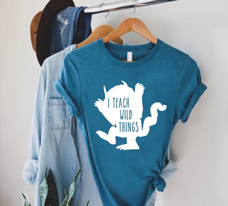 May include: A teal blue t-shirt with a white silhouette of a monster and the text "I teach wild things".
