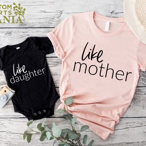 以下が含まれることがあります： 「like mother」と書かれたピンクのTシャツと、「like daughter」と書かれた黒いボディスーツ。