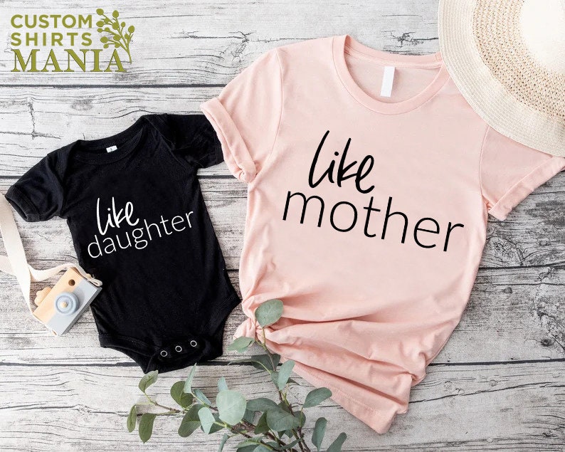 以下が含まれることがあります： 「like mother」と書かれたピンクのTシャツと、「like daughter」と書かれた黒いボディスーツ。