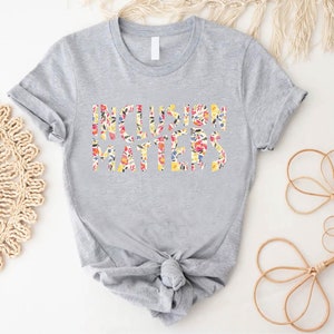 Puede incluir: Una camiseta gris con el texto "Inclusion Matters" impreso en letras florales.