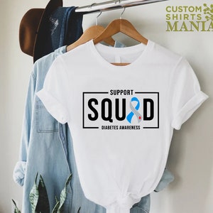 May include: White t-shirt with a black box that says "Support Squad" with a blue ribbon and the words "Diabetes Awareness" underneath.