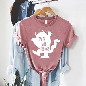 May include: A pink t-shirt with a white silhouette of the Where the Wild Things Are monster and the text "I teach wild things".