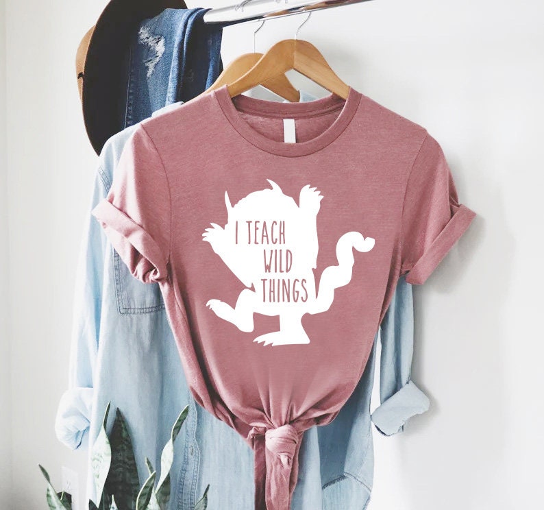 May include: A pink t-shirt with a white silhouette of the Where the Wild Things Are monster and the text "I teach wild things".