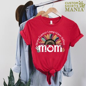 May include: Red t-shirt featuring a white graphic of a sunflower with a leopard print centre and the word "mom" in white with flowers around it. The text around the sunflower reads "Strong, Fearless, Loving, Warm, Selfless".