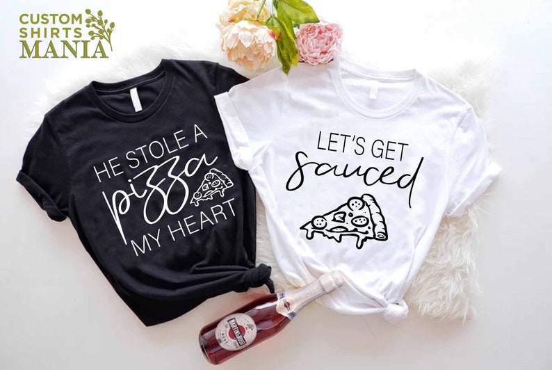 Puede incluir: Dos camisetas blancas y negras con un gr&aacute;fico de pizza y texto. La camiseta negra dice "Se rob&oacute; una pizza de mi coraz&oacute;n" y la camiseta blanca dice "Vamos a emborracharnos".