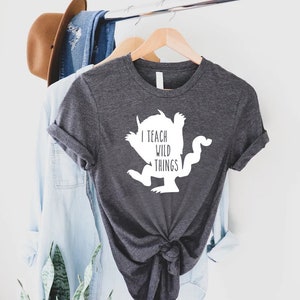 May include: A dark gray t-shirt with a white silhouette of a monster and the text "I teach wild things".