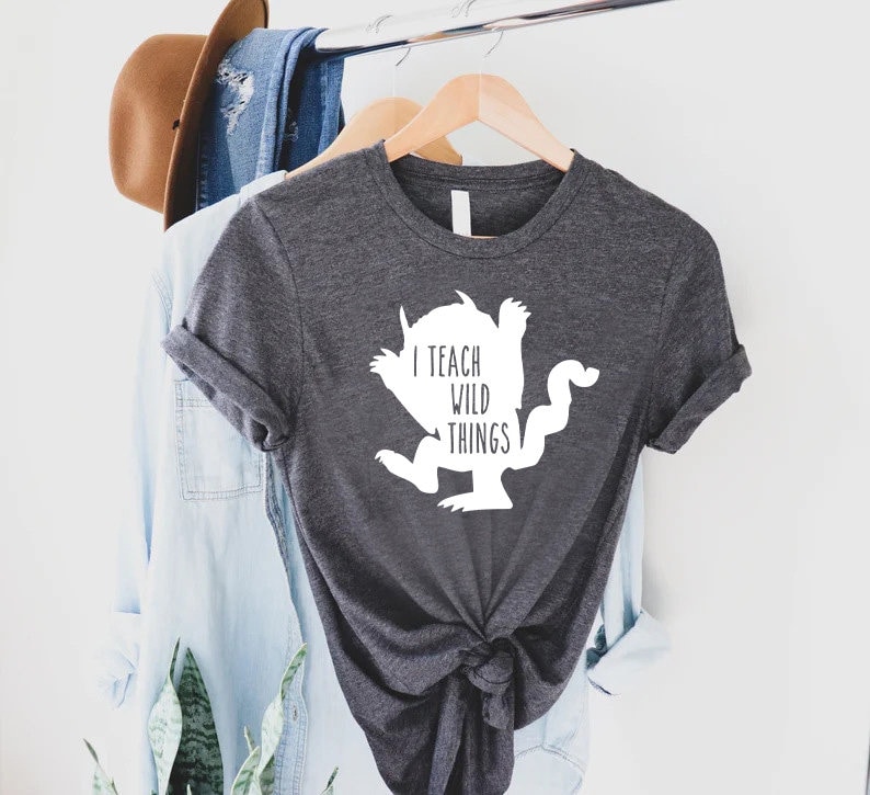 May include: A dark gray t-shirt with a white silhouette of a monster and the text "I teach wild things".