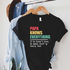 May include: Black t-shirt with the text "PAPA KNOWS EVERYTHING" in red, yellow, and teal. The shirt also includes the text "If he doesn't know, he makes stuff up really fast."