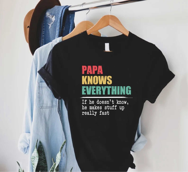 May include: Black t-shirt with the text "PAPA KNOWS EVERYTHING" in red, yellow, and teal. The shirt also includes the text "If he doesn't know, he makes stuff up really fast."