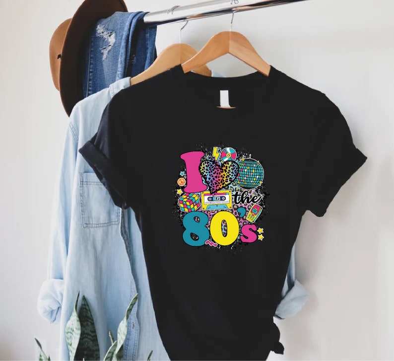 May include: Black t-shirt with a graphic print of a heart with a leopard print, a cassette tape, a disco ball, and the text "I love the 80's".