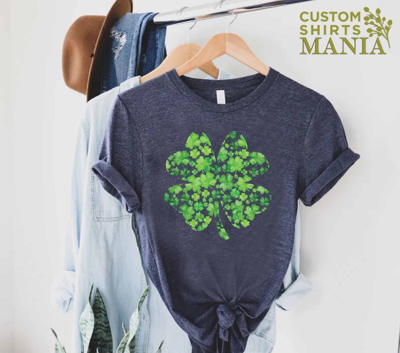 May include: A navy blue t-shirt with a green four-leaf clover design made of smaller clovers. The clover is a popular symbol of good luck and is often associated with St. Patrick's Day.