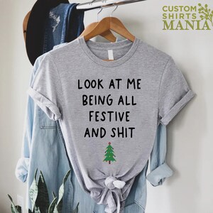 May include: Gray t-shirt with the text "Look at me being all festive and shit" and a small green Christmas tree graphic.