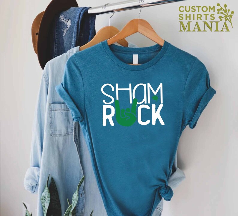 Peut inclure: Un t-shirt bleu sarcelle avec le texte "Shamrock" et un geste de main rock and roll vert.