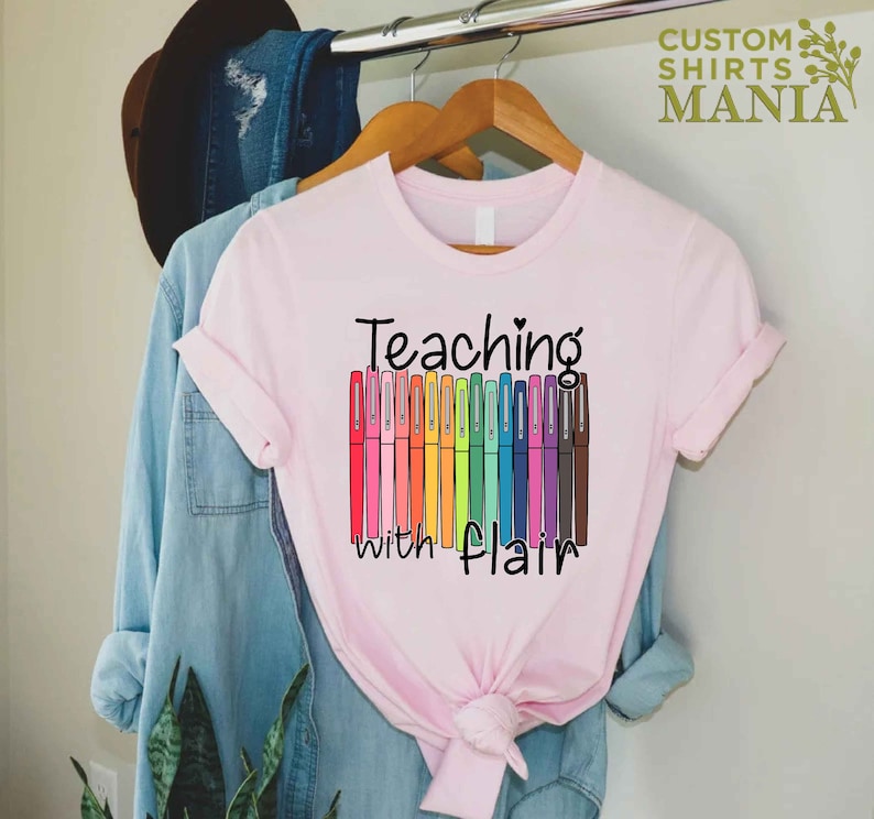 May include: Pink t-shirt with the text "Teaching with flair" and a row of colorful markers.