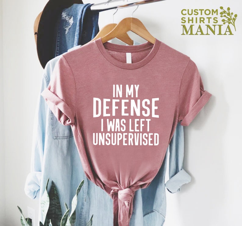 May include: A pink t-shirt with the text "In my defense I was left unsupervised" printed in white.