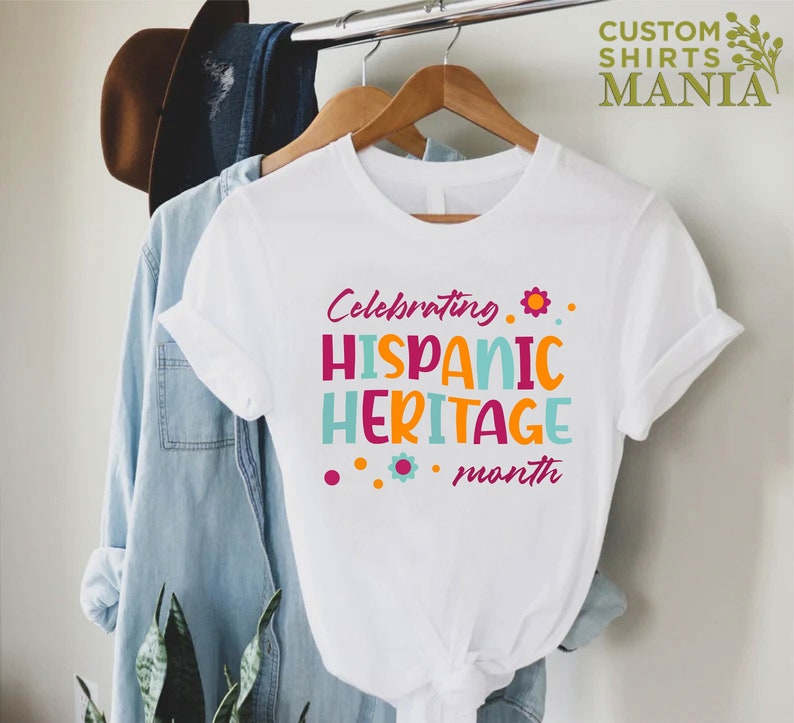 May include: White t-shirt with the text "Celebrating Hispanic Heritage month" in colorful letters and flowers.