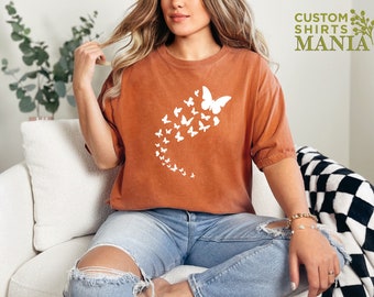May include: A rust-colored t-shirt with a white graphic of a swarm of butterflies. The shirt is made of a soft, comfortable material and has a relaxed fit.