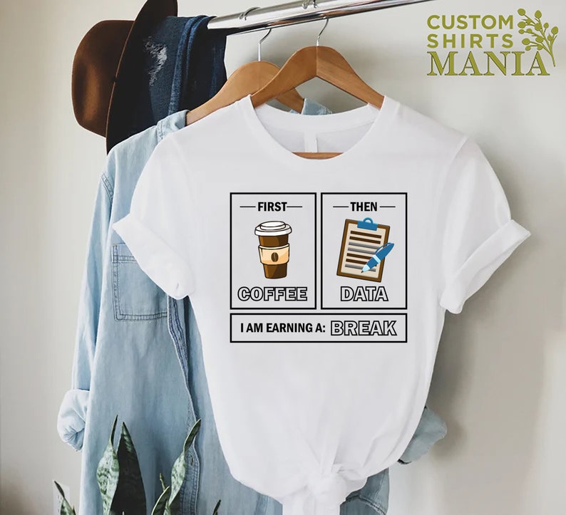 May include: White t-shirt with a graphic of a coffee cup and a clipboard with a pen. The text reads "First - Coffee, Then - Data, I am earning a: Break".