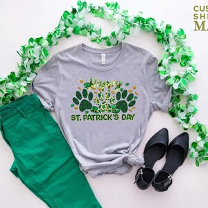 May include: A gray t-shirt with a green shamrock and paw print design. The shirt says "Happy St. Patrick's Day".