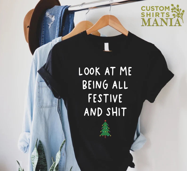 May include: Black t-shirt with white text that reads "Look at me being all festive and shit" and a green Christmas tree with lights.