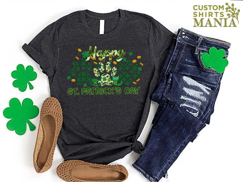 May include: A dark grey t-shirt with a green shamrock and paw print design. The text "Happy St. Patrick's Day" is printed on the shirt.