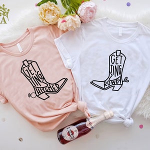 May include: Two white t-shirts with black boot designs and text. One shirt says "Getting Hitched" and the other says "Getting Rowdy".