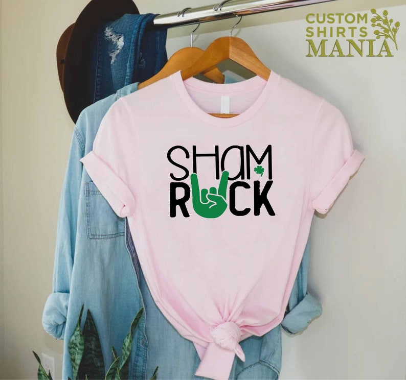 Peut inclure: T-shirt rose avec un texte noir qui dit "Shamrock" avec un geste de main rock and roll vert et un tr&egrave;fle.