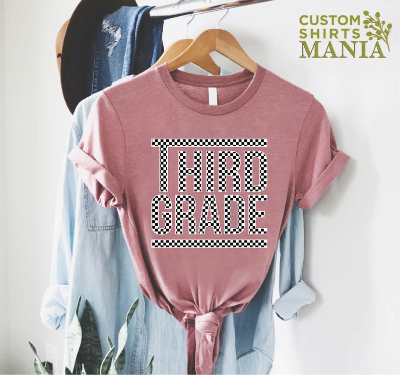 Pu&ograve; includere: Una maglietta rosa con un design a scacchi bianco e nero che dice "TERZA CLASSE" su di essa.