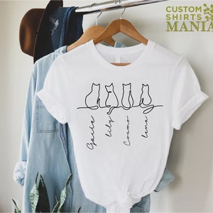 May include: White t-shirt with a line drawing of four cats and the names "Gracie", "Lily", "Cosmo", and "Lena" written underneath.