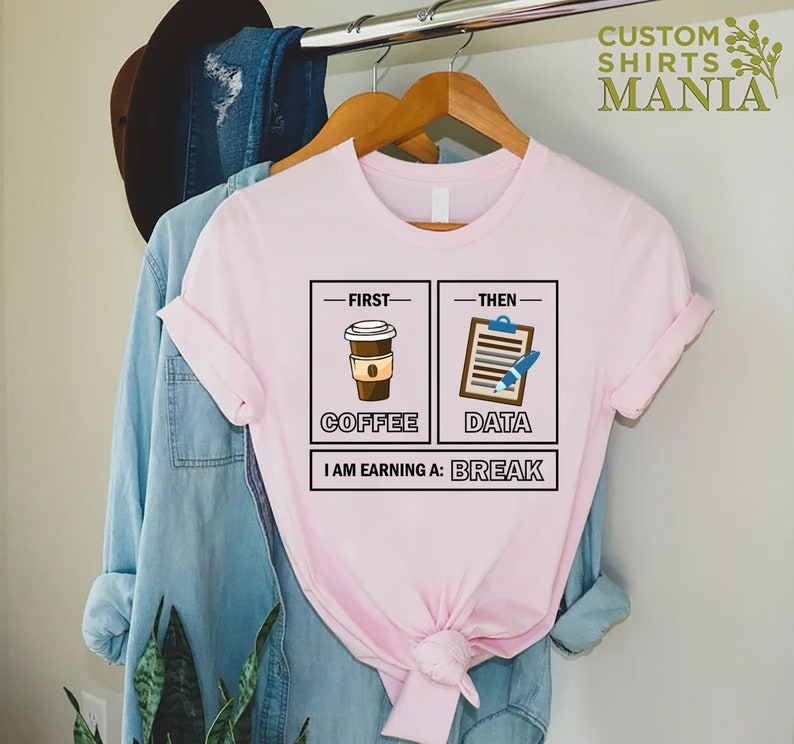 May include: Pink t-shirt with a graphic design that says "First Coffee, Then Data, I am earning a Break". The graphic features a cup of coffee and a clipboard with a pen.