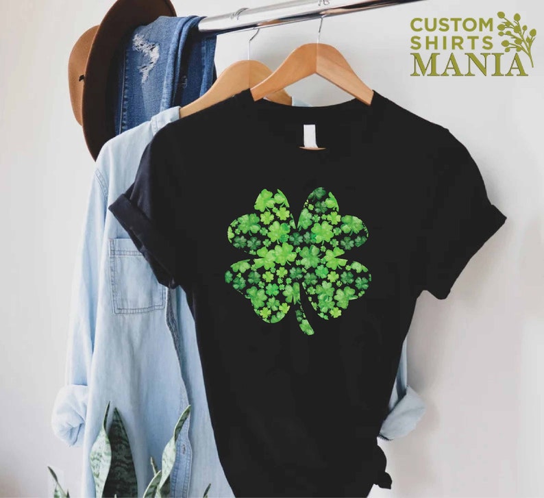 May include: Black t-shirt with a green four-leaf clover design made of smaller clovers. The clover is centered on the shirt.
